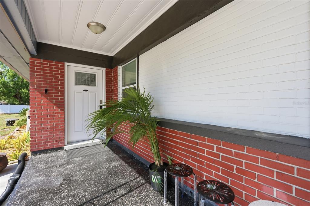 A covered front porch features a white door, red brick walls, and a white-painted brick section — 10107 N ASTER AVENUE, TAMPA, FL