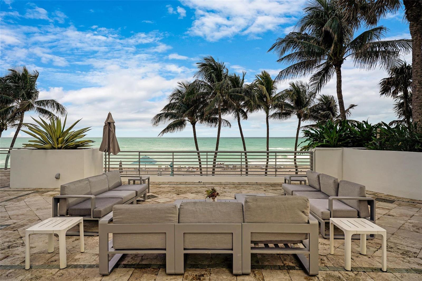 A stone patio features outdoor seating facing a beach, ocean, and palm trees — 3535 S Ocean Drive # 402, Hollywood FL 33019, HOLLYWOOD, FL