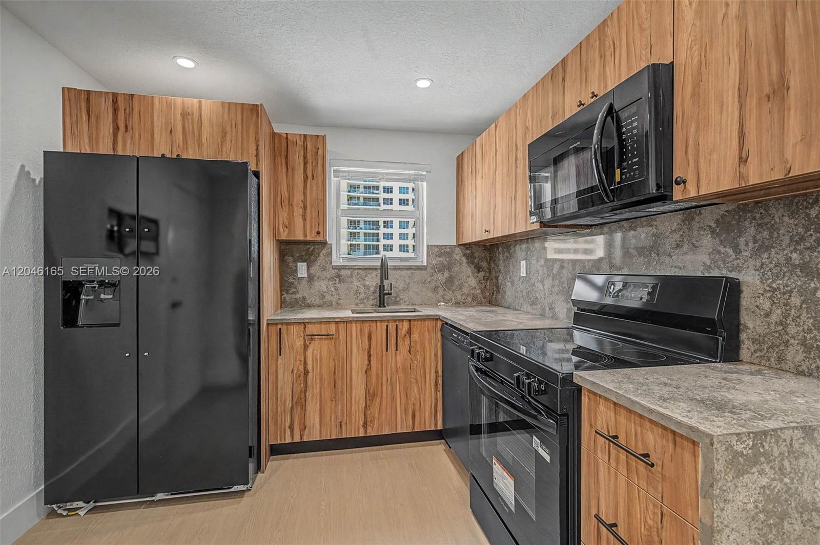 A kitchen features wood-grain cabinets, black appliances, and a gray stone-look countertop and backsplash — 5555 Collins Ave # 7B, Miami Beach FL 33140, MIAMI BEACH, FL