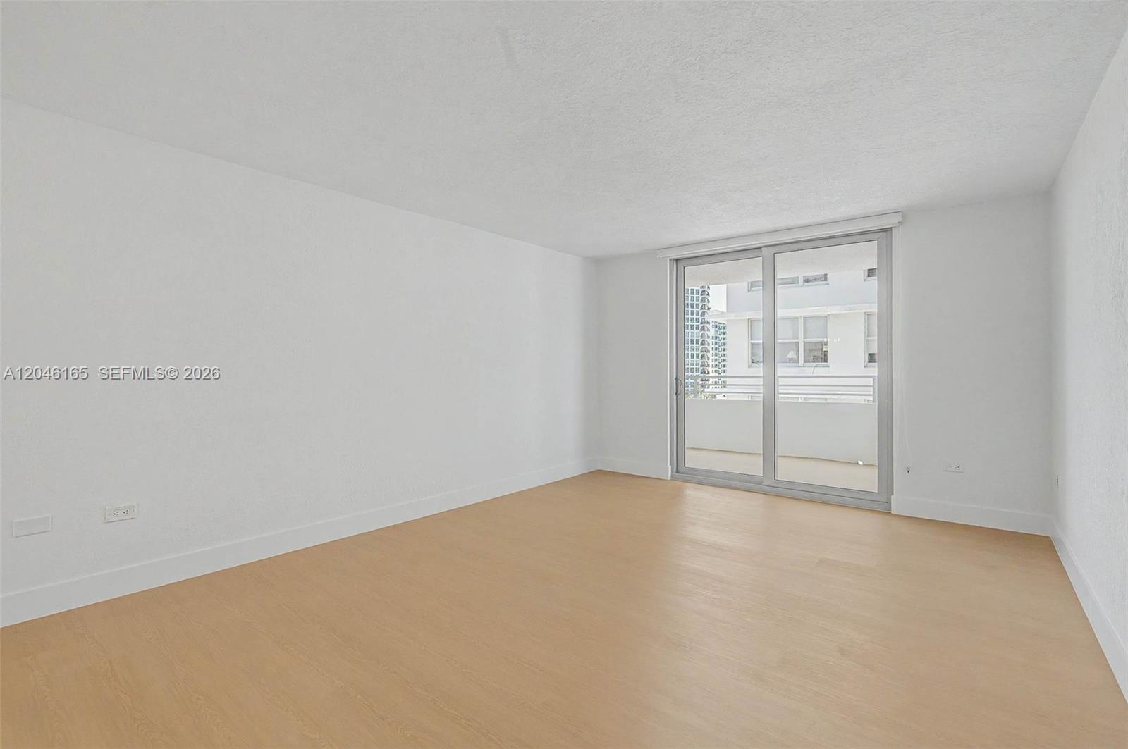 An empty room features white walls, light wood-look flooring, and a sliding glass door — 5555 Collins Ave # 7B, Miami Beach FL 33140, MIAMI BEACH, FL