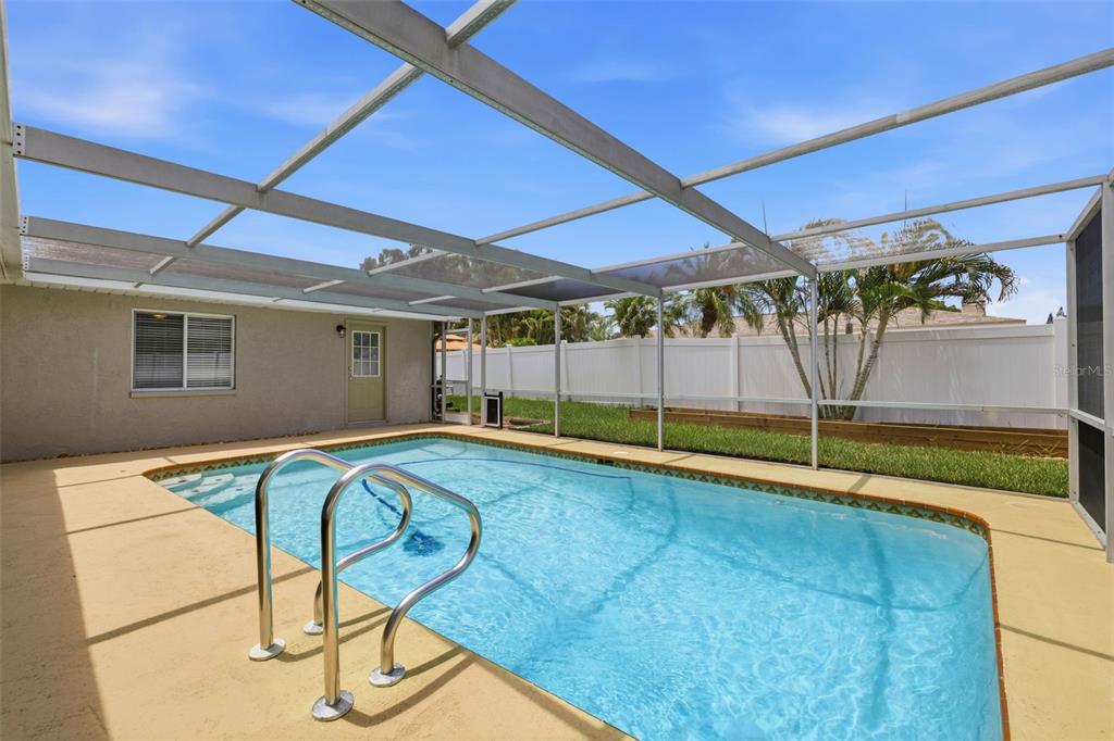 A screened-in swimming pool with a metal handrail sits on a beige patio — 2778 BRATTLE LANE, CLEARWATER, FL