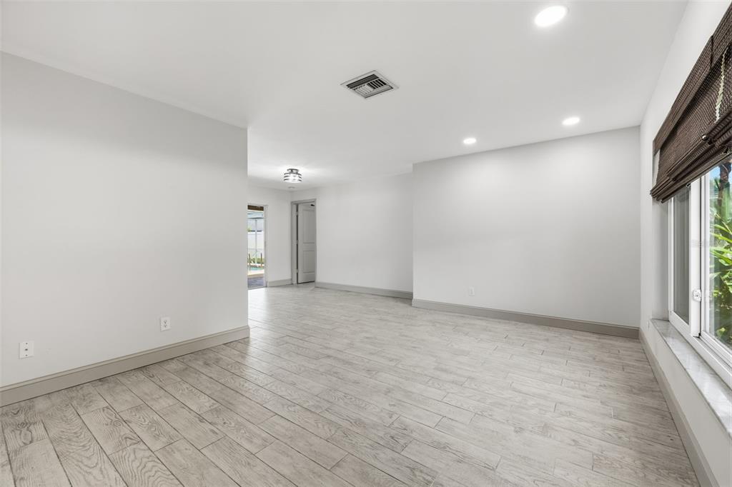 A bright, empty room with light wood-look tile flooring, white walls, and a large window — 2778 BRATTLE LANE, CLEARWATER, FL