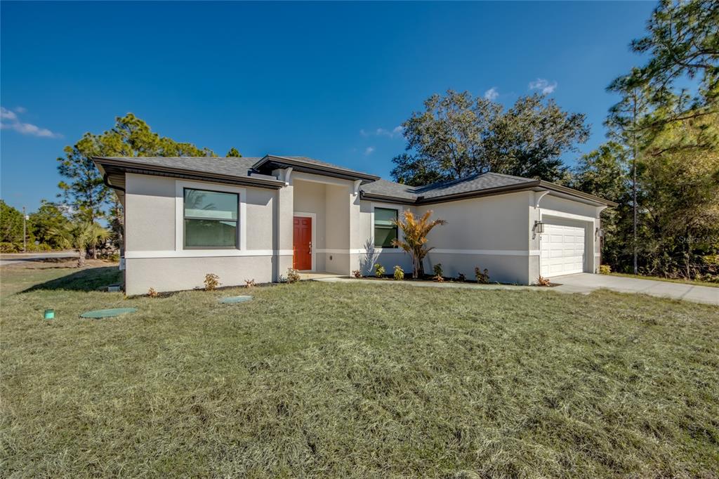 A single-story house with a light-colored stucco exterior, a red front door, and a garage — 2512 48TH STREET W, LEHIGH ACRES, FL