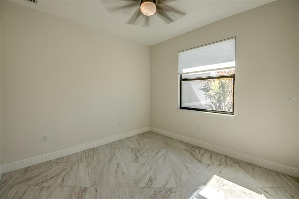 An empty room with light-colored walls, a ceiling fan, and white marble-patterned tile flooring — 2512 48TH STREET W, LEHIGH ACRES, FL