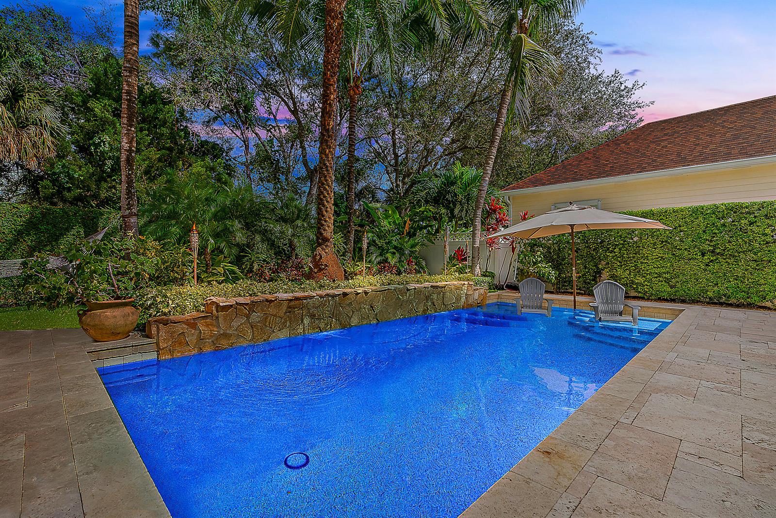 A rectangular swimming pool with a stone wall feature and two chairs in the water — 140 Sweet Bay Circle, Jupiter FL 33458, JUPITER, FL