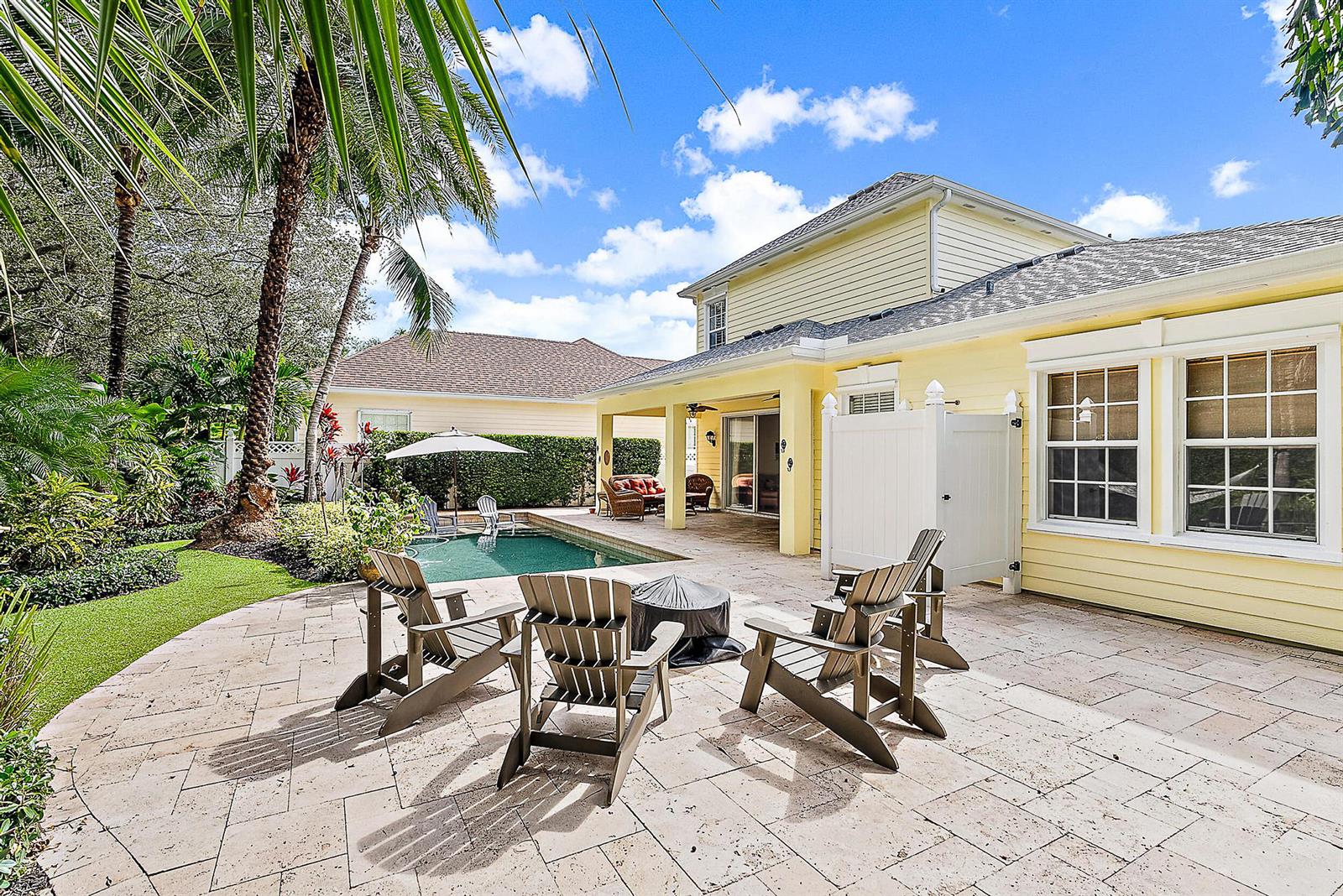 A yellow house features a stone patio with Adirondack chairs, a fire pit, and pool — 140 Sweet Bay Circle, Jupiter FL 33458, JUPITER, FL