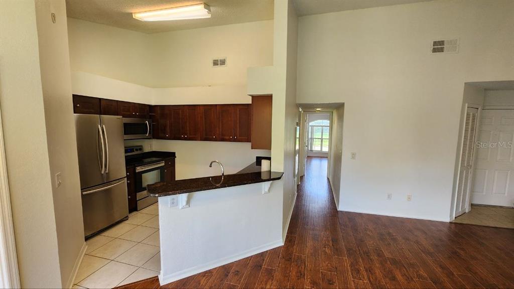 A kitchen with dark wood cabinets and stainless steel appliances overlooks a wood-floored living area — 4623 GATE PLACE UNIT 206, ORLANDO, FL