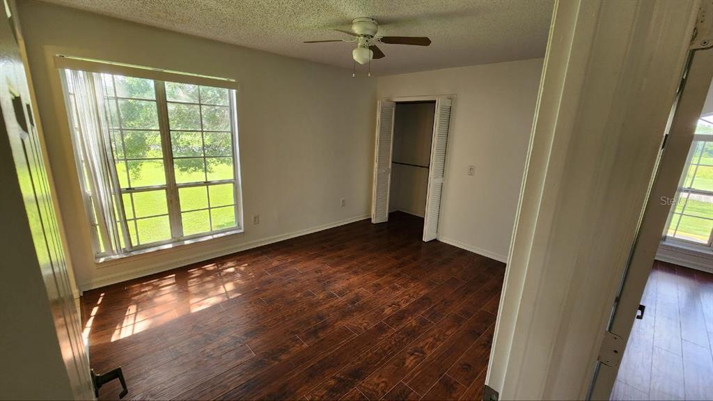 A bedroom with wood-look flooring, a ceiling fan, a closet, and a large window — 4623 GATE PLACE UNIT 206, ORLANDO, FL