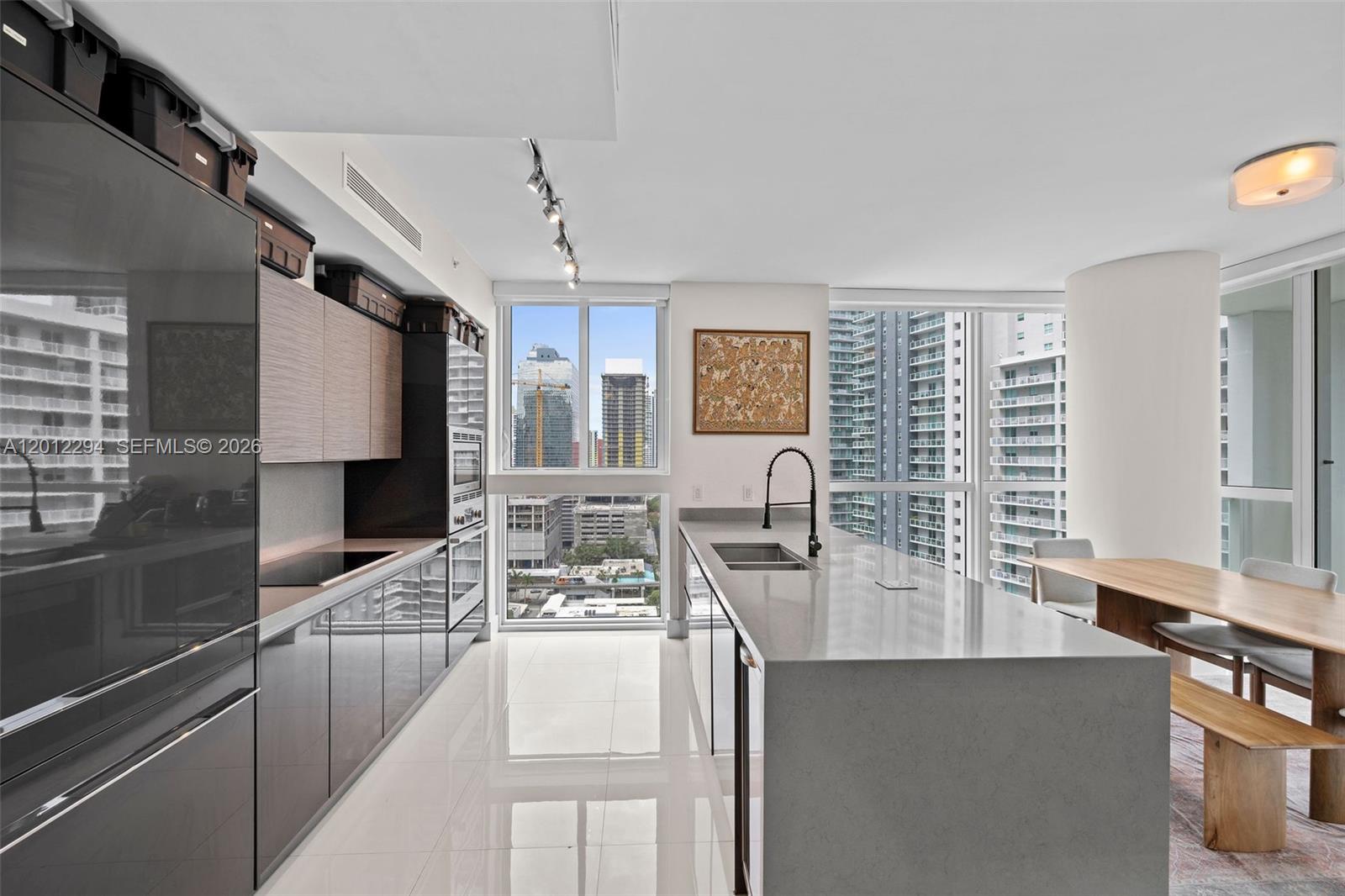 A modern kitchen features gray cabinetry, a large stone island, and floor-to-ceiling city views — 1080 Brickell Ave # 2001, Miami FL 33131, MIAMI, FL