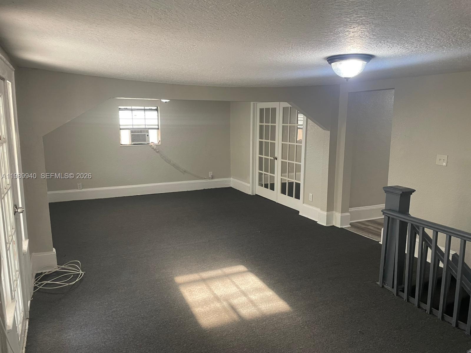 An empty carpeted room features a sloped ceiling, French doors, and a small window unit — 1129 Grothe St, Jacksonville FL 32209, JACKSONVILLE, FL