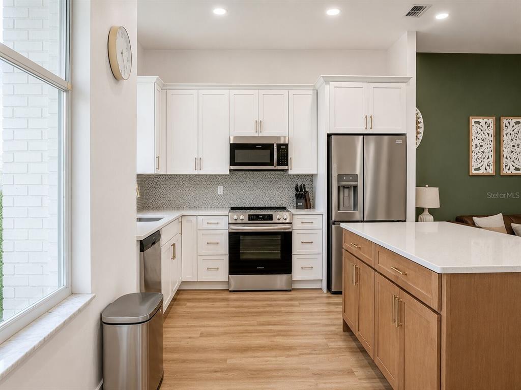 A kitchen features white cabinets, stainless steel appliances, a wood-toned island, and light wood flooring — 297 N LAKE JESSUP AVENUE, OVIEDO, FL