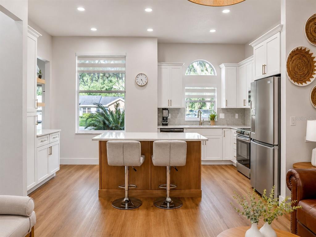 A modern kitchen features white cabinetry, a wood-toned island with two stools, and stainless appliances — 297 N LAKE JESSUP AVENUE, OVIEDO, FL