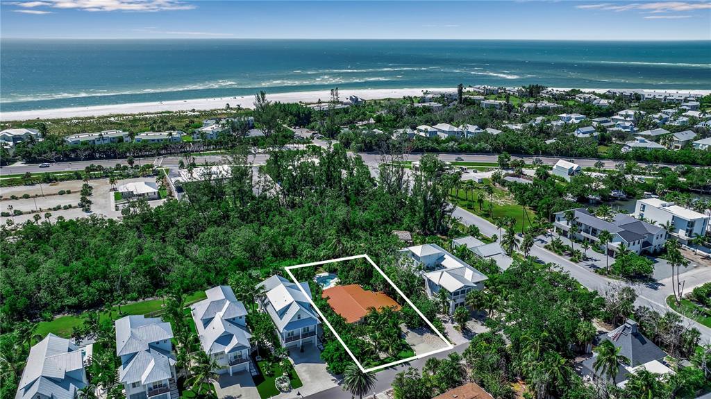 An aerial view shows a house with a red roof surrounded by trees near the ocean — 6979 LONGBOAT DRIVE S, LONGBOAT KEY, FL