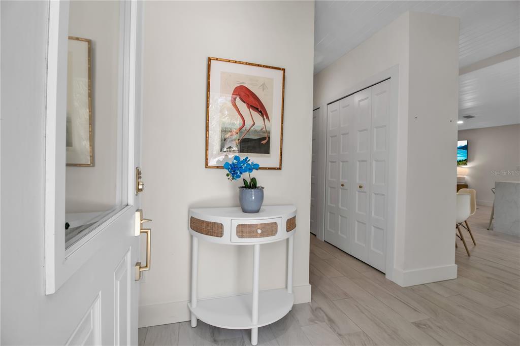 A white entryway features a semi-circular console table, a flamingo print, and light wood flooring — 6979 LONGBOAT DRIVE S, LONGBOAT KEY, FL