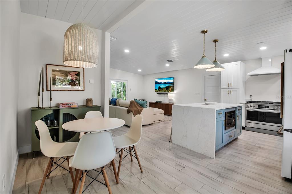 An open-concept kitchen and dining area features white cabinetry, a blue island, and wood-look flooring — 6979 LONGBOAT DRIVE S, LONGBOAT KEY, FL
