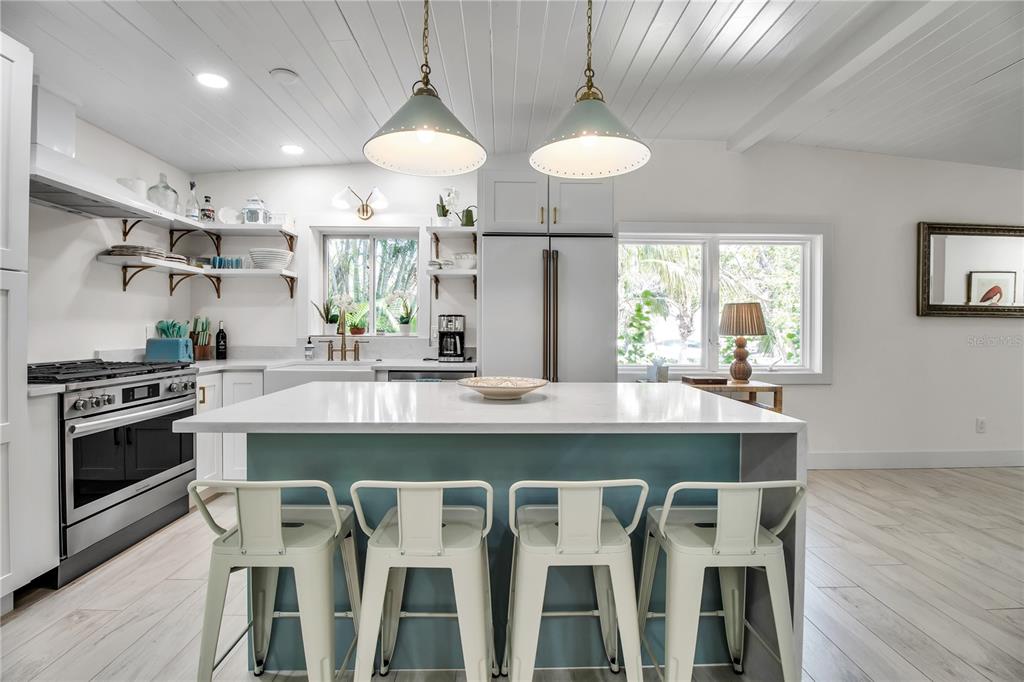 A bright kitchen features a blue island with four white stools and white cabinetry — 6979 LONGBOAT DRIVE S, LONGBOAT KEY, FL