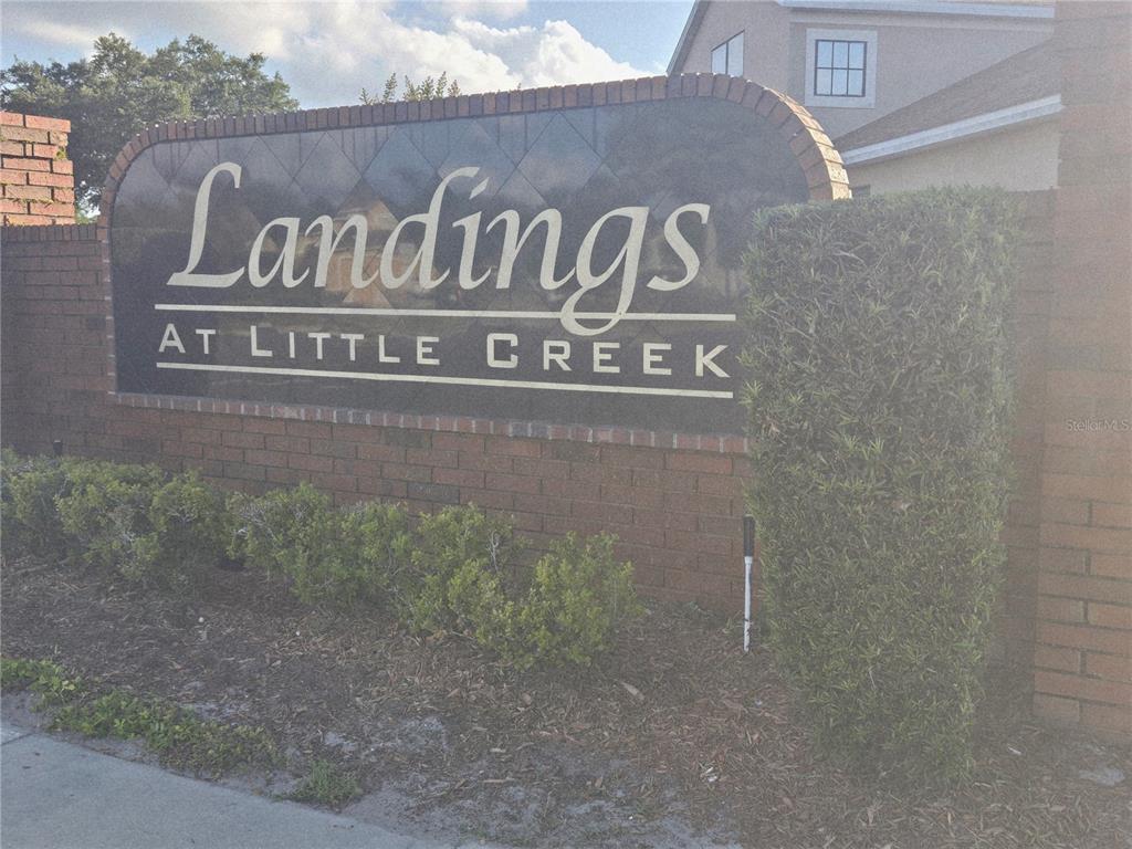 A brick wall displays a sign for Landings at Little Creek with landscaping in front — 1651 RIVER BIRCH AVENUE, OVIEDO, FL
