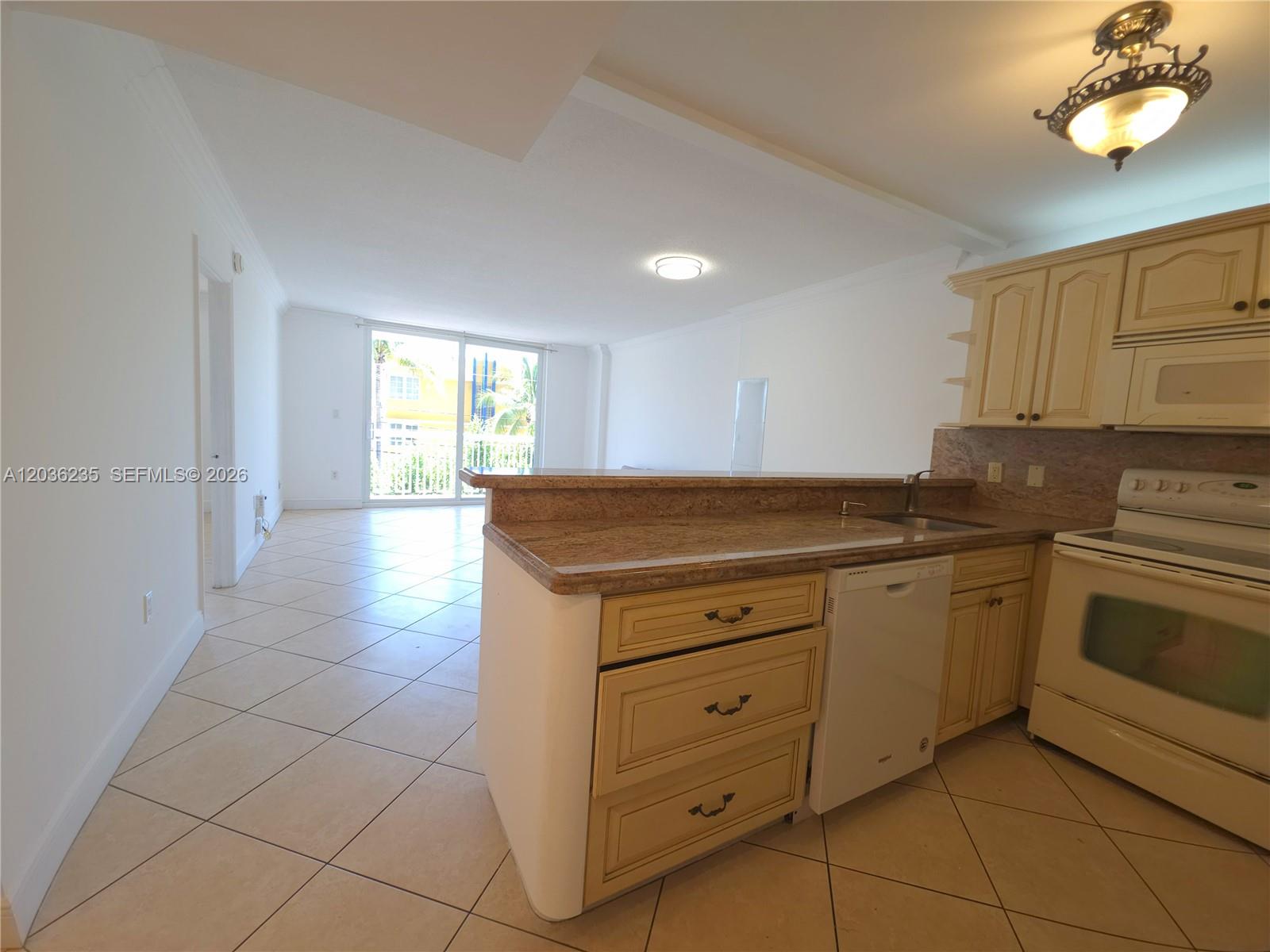 A kitchen with light-colored cabinets and granite countertops overlooks an open living area — 401 Ocean Dr # 304, Miami Beach FL 33139, MIAMI BEACH, FL