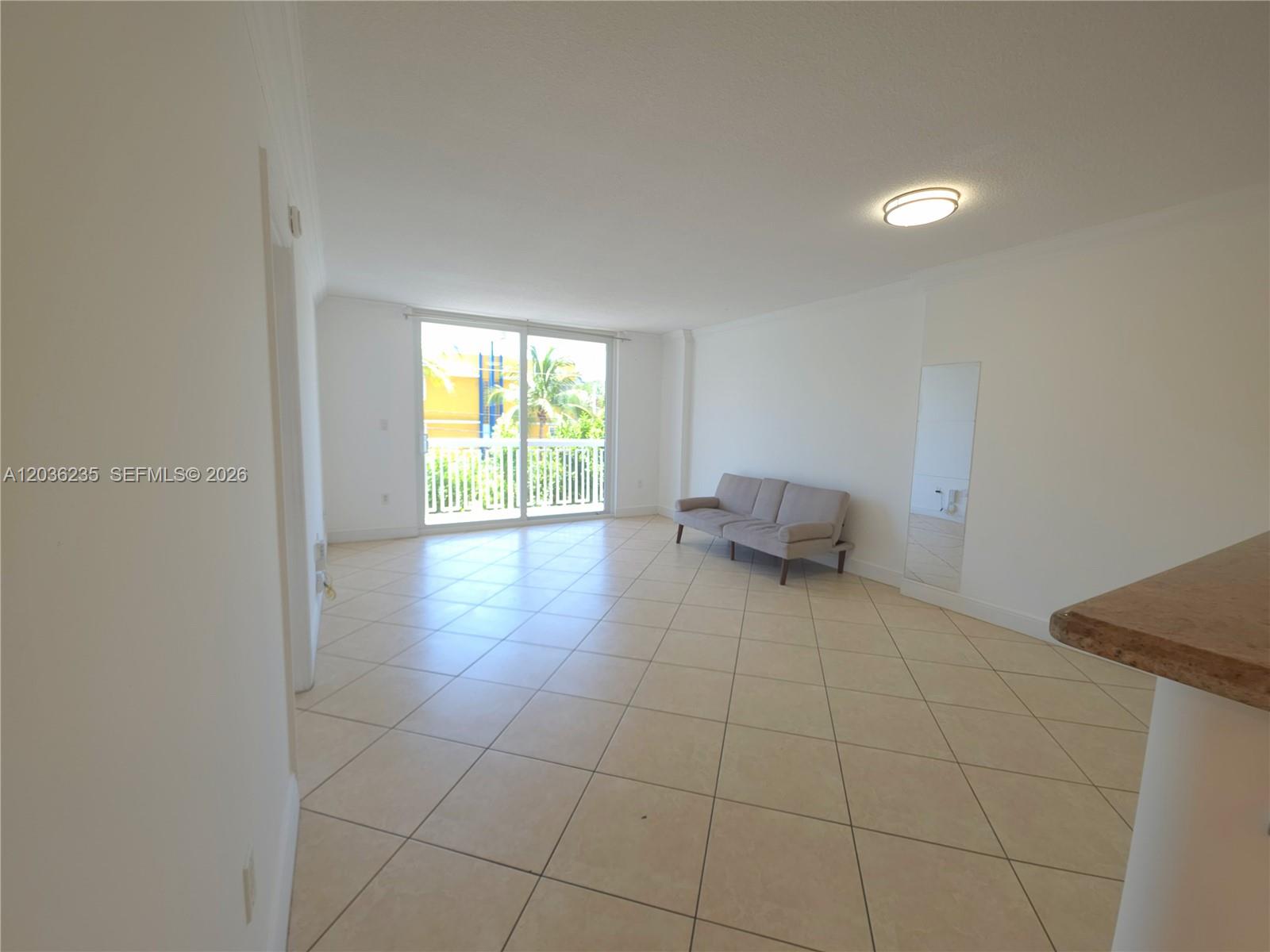 An empty living room features beige tile flooring, white walls, and a sliding glass door — 401 Ocean Dr # 304, Miami Beach FL 33139, MIAMI BEACH, FL