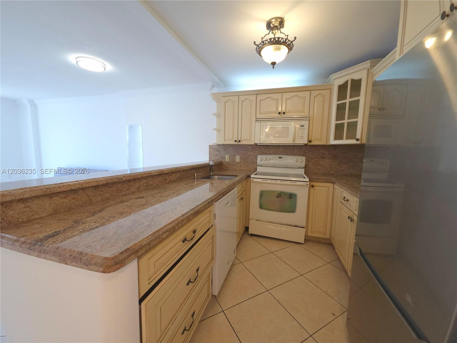 A kitchen features cream-colored cabinets, granite countertops, white appliances, and diagonal tile flooring — 401 Ocean Dr # 304, Miami Beach FL 33139, MIAMI BEACH, FL