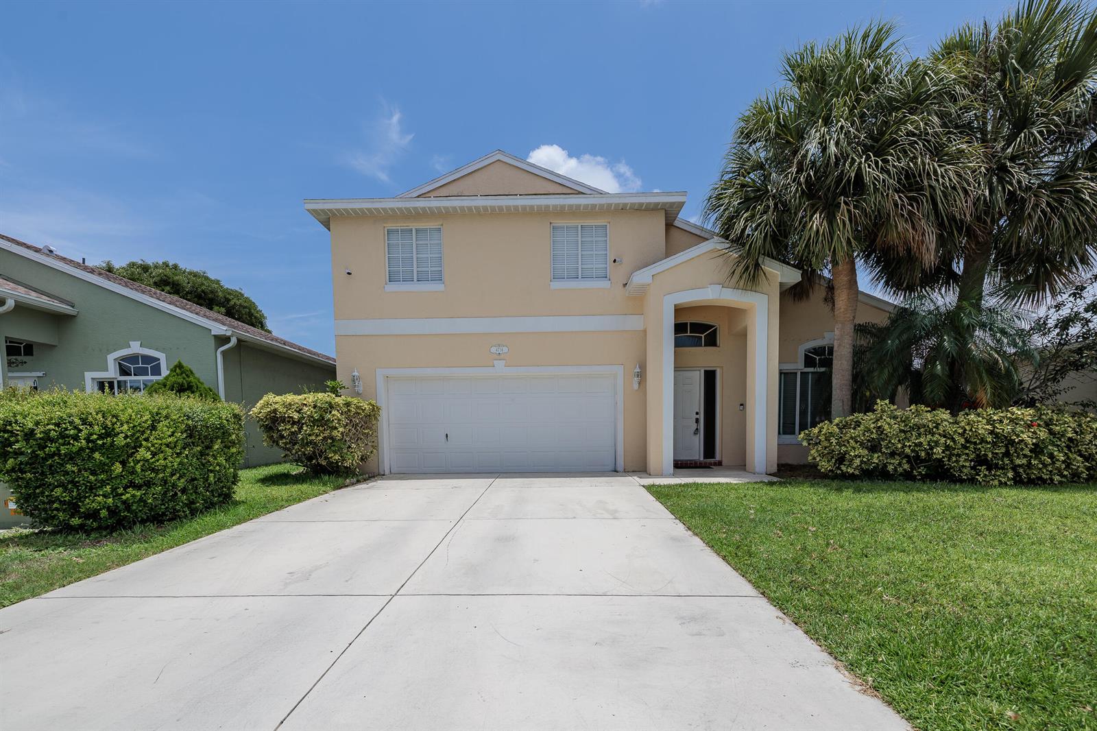 A two-story, beige suburban house features a two-car garage, a palm tree, and landscaping — 4716 SE Winter Haven Court, Stuart FL 34997, STUART, FL