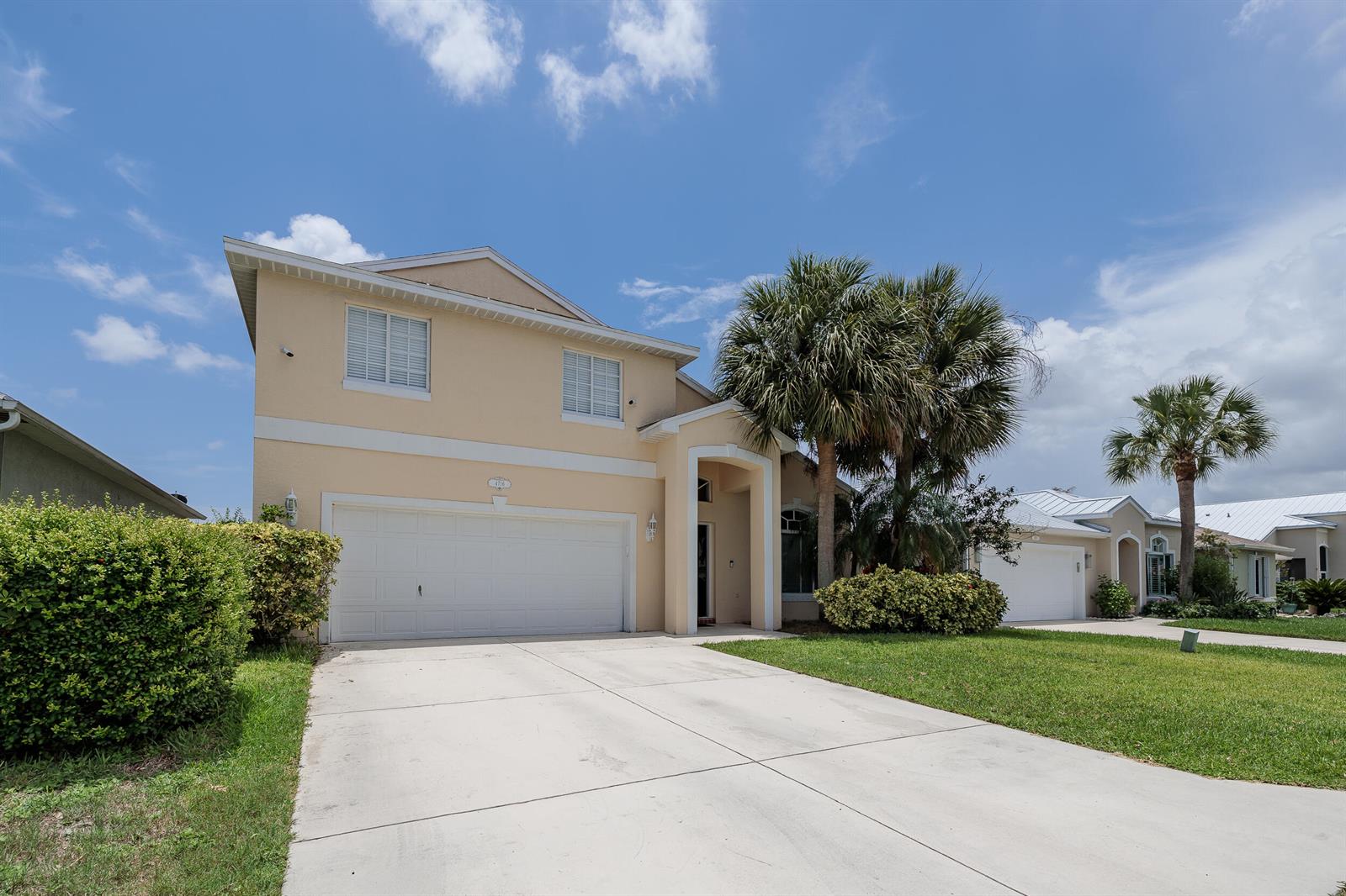A two-story beige house with a two-car garage and palm trees in the front yard — 4716 SE Winter Haven Court, Stuart FL 34997, STUART, FL