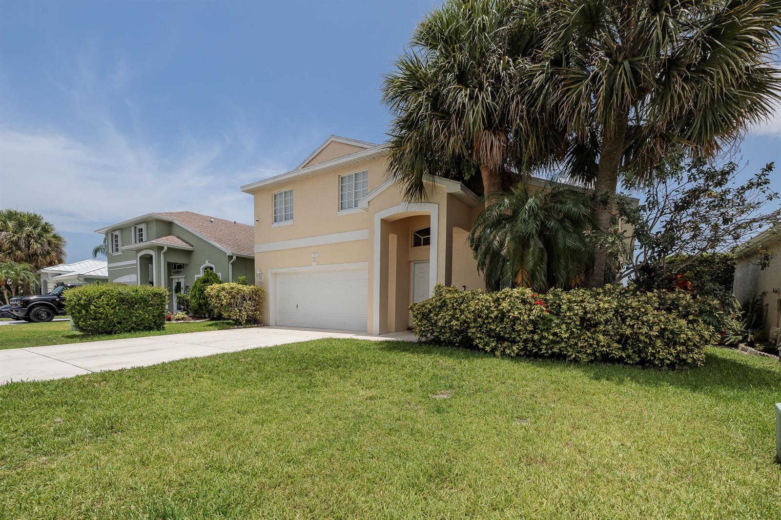 A two-story beige house with a two-car garage and a large palm tree in front — 4716 SE Winter Haven Court, Stuart FL 34997, STUART, FL