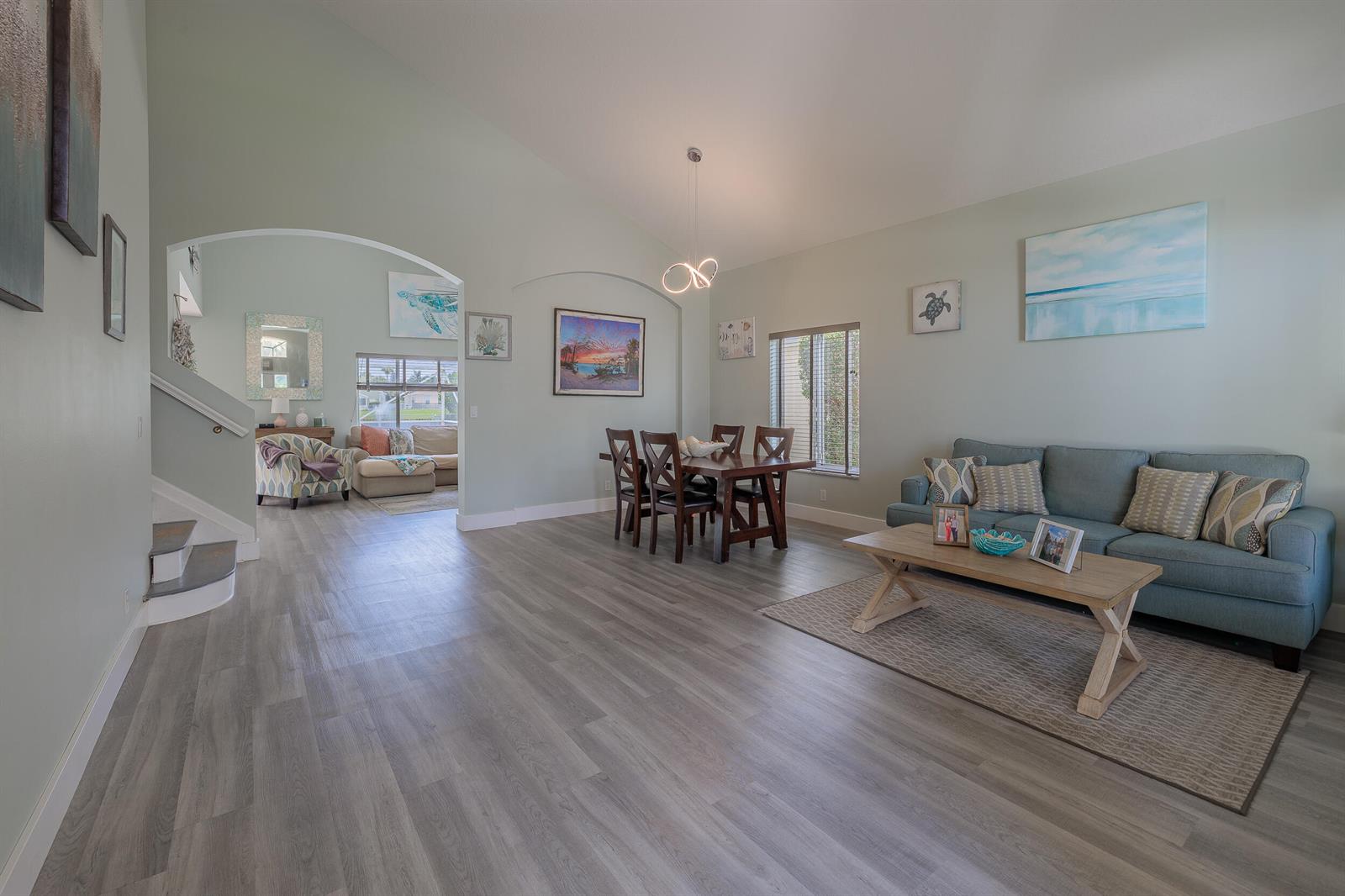 An open-concept living and dining area features light green walls, wood-look flooring, and vaulted ceilings — 4716 SE Winter Haven Court, Stuart FL 34997, STUART, FL