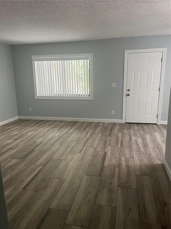 An empty room with light gray walls, wood-look tile flooring, a window, and a door — 3300 FOX CHASE CIRCLE N UNIT 213, PALM HARBOR, FL
