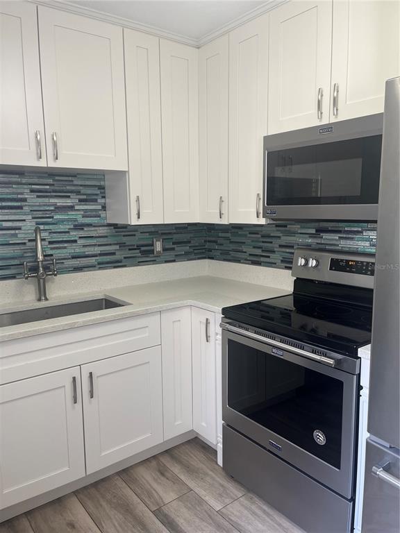 A kitchen features white cabinets, stainless steel appliances, a blue glass tile backsplash, and countertops — 3300 FOX CHASE CIRCLE N UNIT 213, PALM HARBOR, FL
