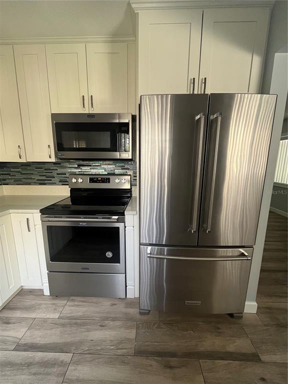 A kitchen features white cabinets, stainless steel appliances, a tiled backsplash, and wood-look floor tiles — 3300 FOX CHASE CIRCLE N UNIT 213, PALM HARBOR, FL