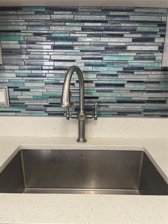 A stainless steel kitchen sink with a gooseneck faucet against a blue glass tile backsplash — 3300 FOX CHASE CIRCLE N UNIT 213, PALM HARBOR, FL