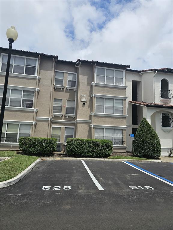 The exterior of a multi-story apartment building features beige stucco walls and numbered parking spaces — 5132 CONROY ROAD UNIT 937, ORLANDO, FL