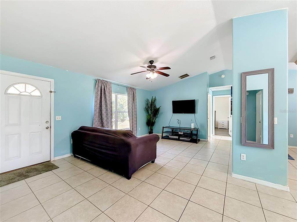 A living room with light blue walls, tile flooring, a ceiling fan, and a dark sofa — 13 BAHIA PASS RUN, OCALA, FL