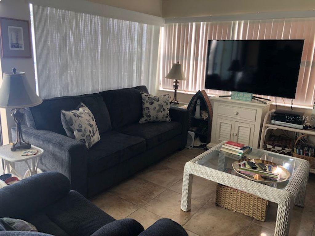 A living room features a dark sofa, a glass-topped wicker coffee table, and a television — 1571 S ATLANTIC AVENUE UNIT 205, NEW SMYRNA BEACH, FL