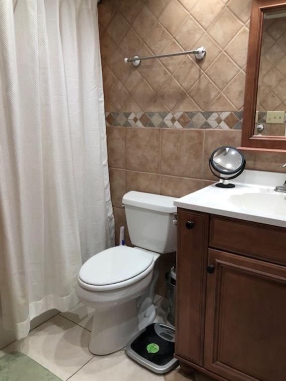 A bathroom features a white toilet, a wooden vanity with a mirror, and tiled walls — 1571 S ATLANTIC AVENUE UNIT 205, NEW SMYRNA BEACH, FL