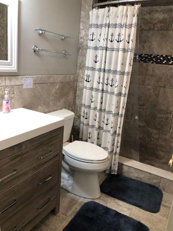 A bathroom features a wood-look vanity, a white toilet, and a shower with anchor-patterned curtains — 1571 S ATLANTIC AVENUE UNIT 205, NEW SMYRNA BEACH, FL