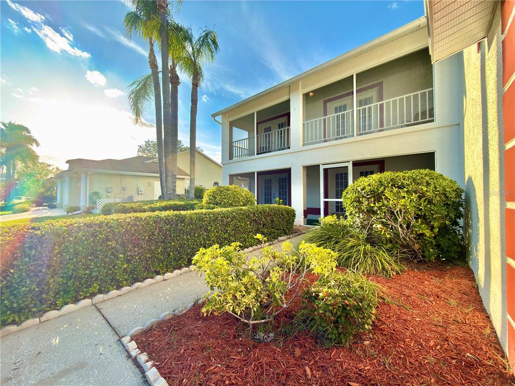 A two-story building with screened balconies and a landscaped walkway in the foreground — 1702 SUNKISSED DRIVE, TARPON SPRINGS, FL