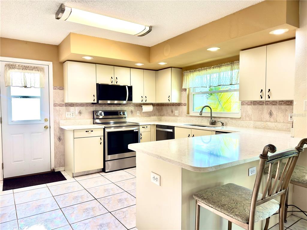 A kitchen with white cabinets, stainless steel appliances, tile flooring, and a breakfast bar — 1702 SUNKISSED DRIVE, TARPON SPRINGS, FL