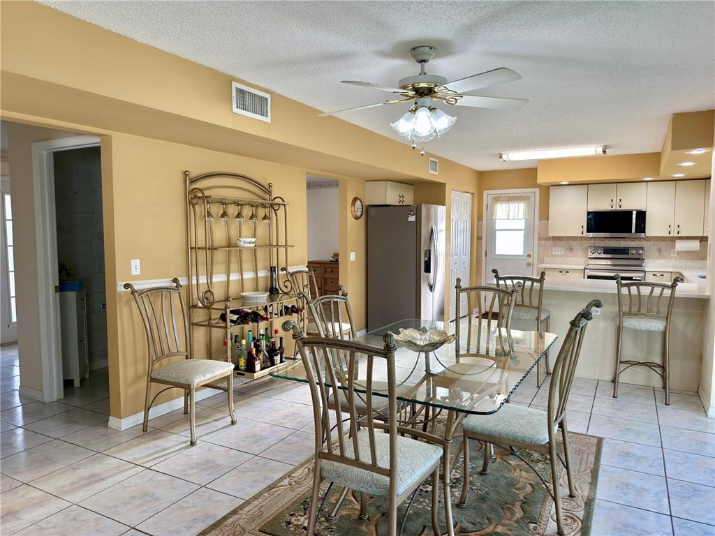 A dining area with a glass table and metal chairs sits adjacent to a kitchen — 1702 SUNKISSED DRIVE, TARPON SPRINGS, FL