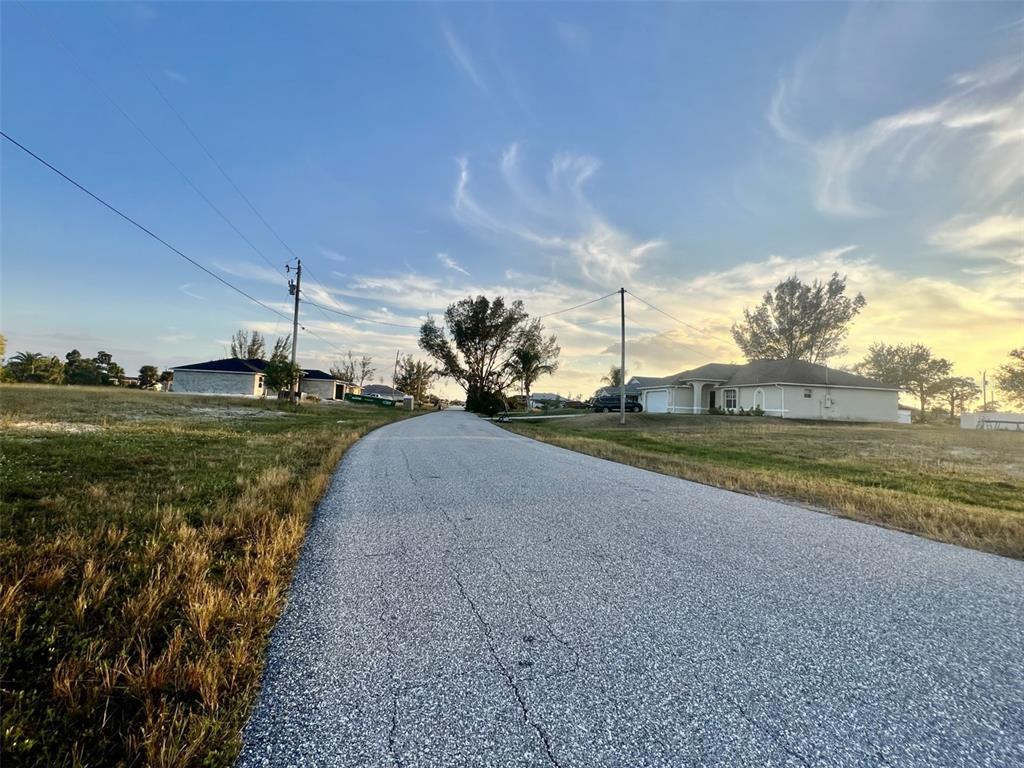 A paved road stretches between grassy lots and houses under a blue sky at sunset — 1213 NW 20TH PLACE, CAPE CORAL, FL