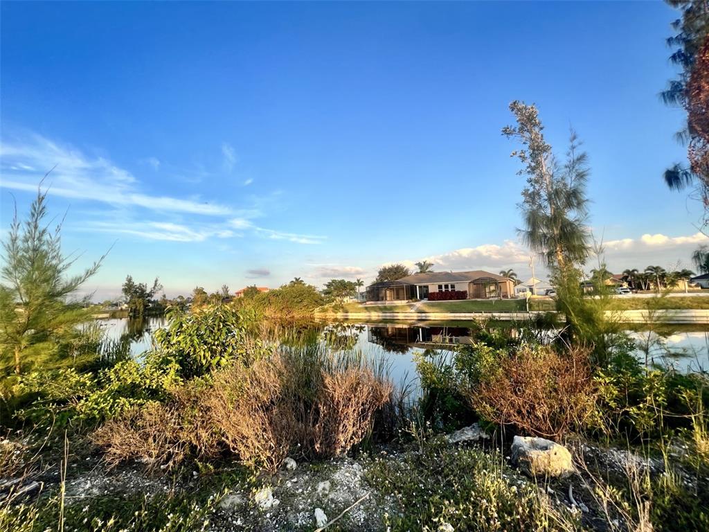 A house with a screened lanai sits across a calm pond surrounded by vegetation — 1213 NW 20TH PLACE, CAPE CORAL, FL