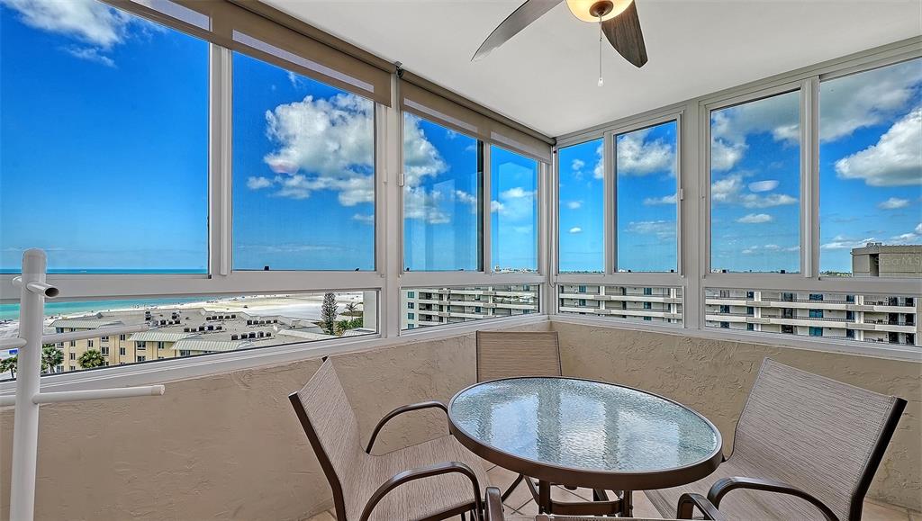 A sunroom features a glass-topped table, chairs, and large windows overlooking a beach — 5920 MIDNIGHT PASS ROAD UNIT 1003, SARASOTA, FL
