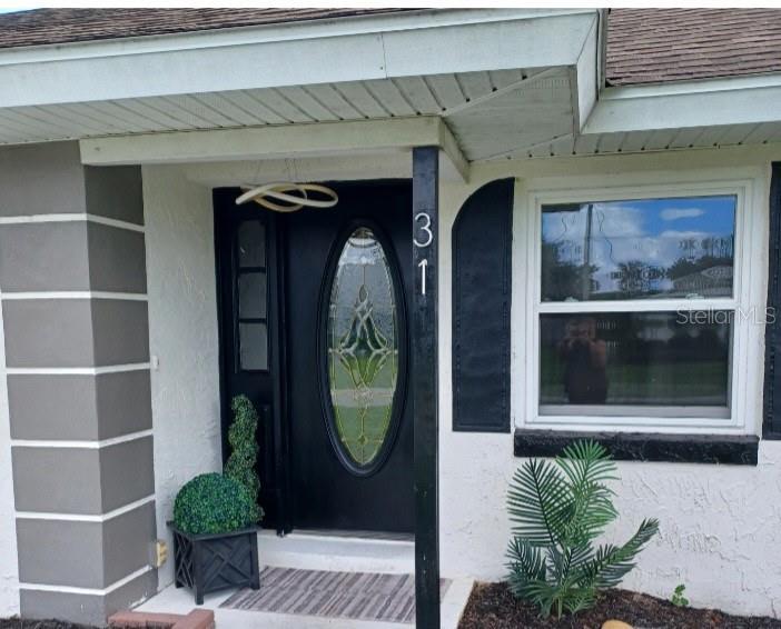 A black front door with an oval glass insert sits under a covered porch — 31 FREELAND LANE, PALM COAST, FL