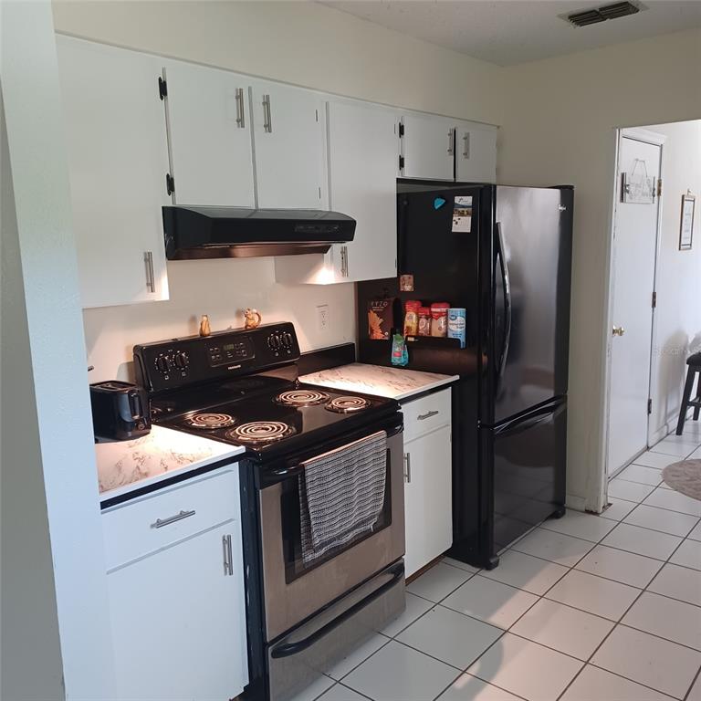 A kitchen features white cabinets, black appliances, a stainless steel stove, and white tiled flooring — 31 FREELAND LANE, PALM COAST, FL