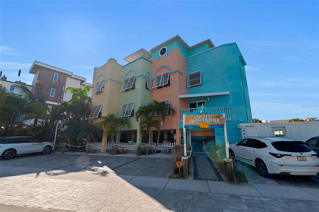 A multi-story, pastel-colored building features a sign for Siesta Sunset Royale and parked cars — 5322 CALLE DE LA SIESTA, SARASOTA, FL