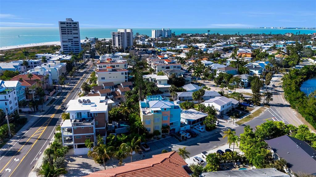 An aerial view shows a coastal neighborhood with multi-story homes, palm trees, and the ocean — 5322 CALLE DE LA SIESTA, SARASOTA, FL