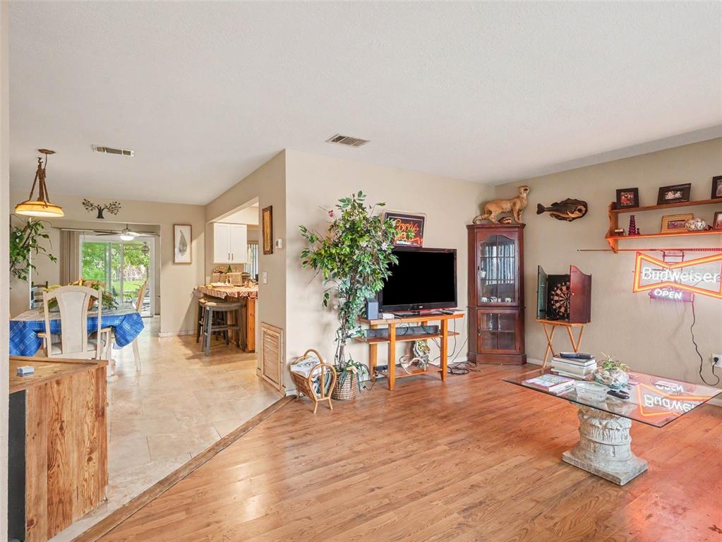 A living room with wood flooring flows into a tiled dining area and kitchen — 6716 DENNISON AVENUE, NORTH PORT, FL