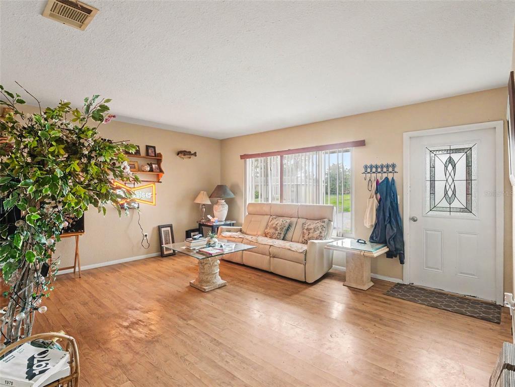 A living room features light-colored walls, wood flooring, a beige sofa, and a front door — 6716 DENNISON AVENUE, NORTH PORT, FL