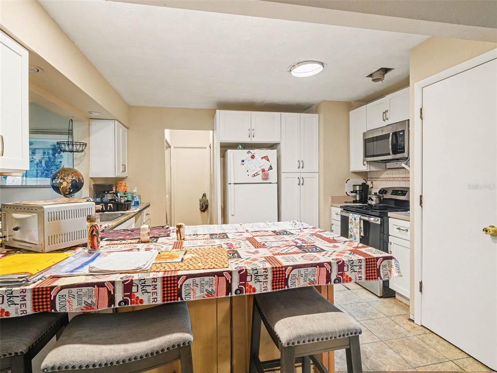 A kitchen features white cabinets, a central island with a patterned tablecloth, and tile flooring — 6716 DENNISON AVENUE, NORTH PORT, FL